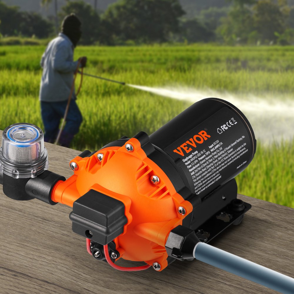 Bomba de diafragma de presión de agua VEVOR 12v en color naranja colocada sobre una mesa, con una persona rociando agua en un campo.