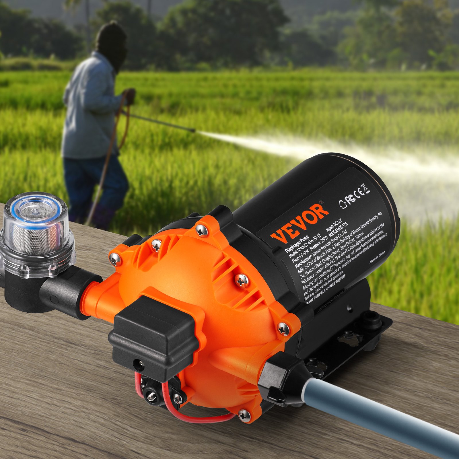 Bomba de diafragma de presión de agua VEVOR 12v en color naranja colocada sobre una mesa, con una persona rociando agua en un campo.