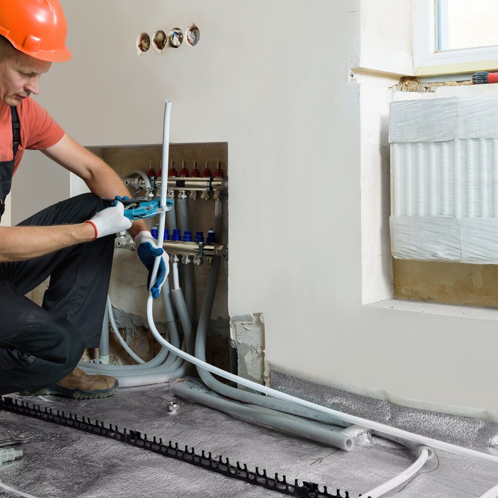 Instalador trabajando en un sistema de calefacción con tubería pex VEVOR, conectando líneas debajo de una ventana con un radiador.