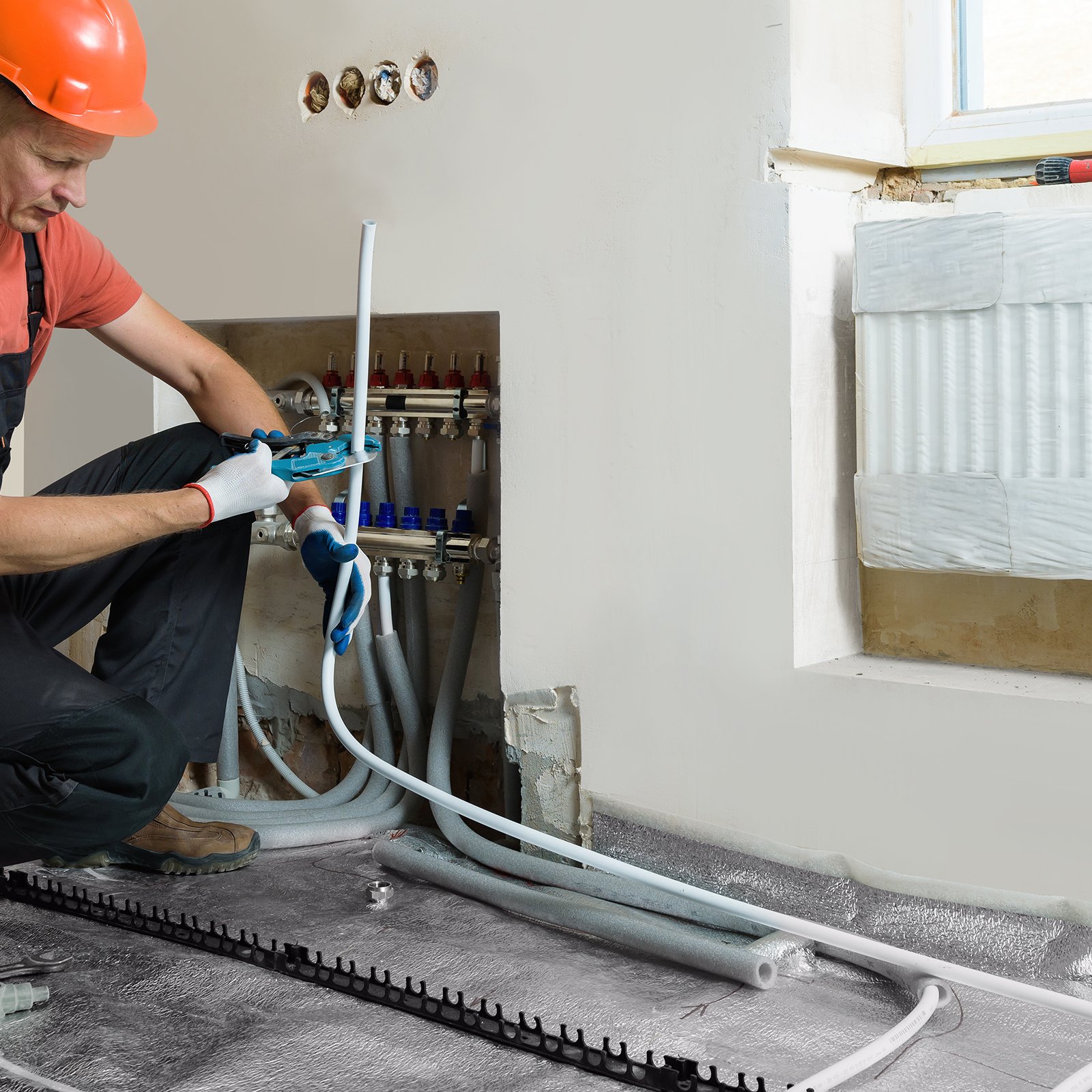 Instalador trabajando en un sistema de calefacción con tubería pex VEVOR, conectando líneas debajo de una ventana con un radiador.
