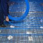 Persona instalando tubería pex azul VEVOR en una rejilla de piso reforzada con acero para calefacción por suelo radiante.