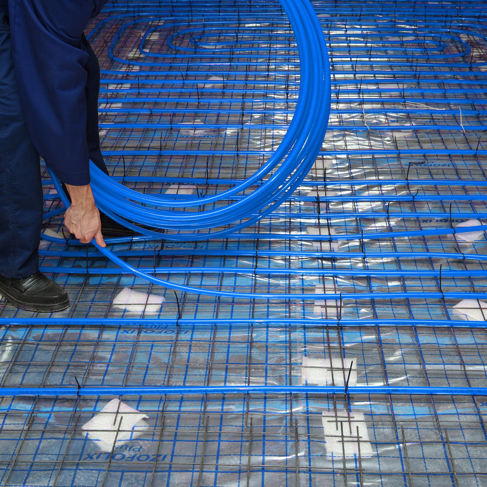 Persona instalando tubería pex azul VEVOR en una rejilla de piso reforzada con acero para calefacción por suelo radiante.