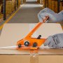 Trabajador de almacén que utiliza el kit de flejado y bandas VEVOR para asegurar una caja de cartón con una correa de plástico.