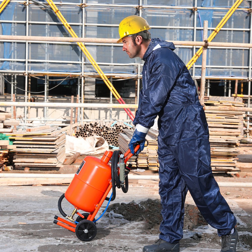 Trabajador con equipo de protección que utiliza una máquina pulidora de arena VEVOR en un sitio de construcción con andamios al fondo.
