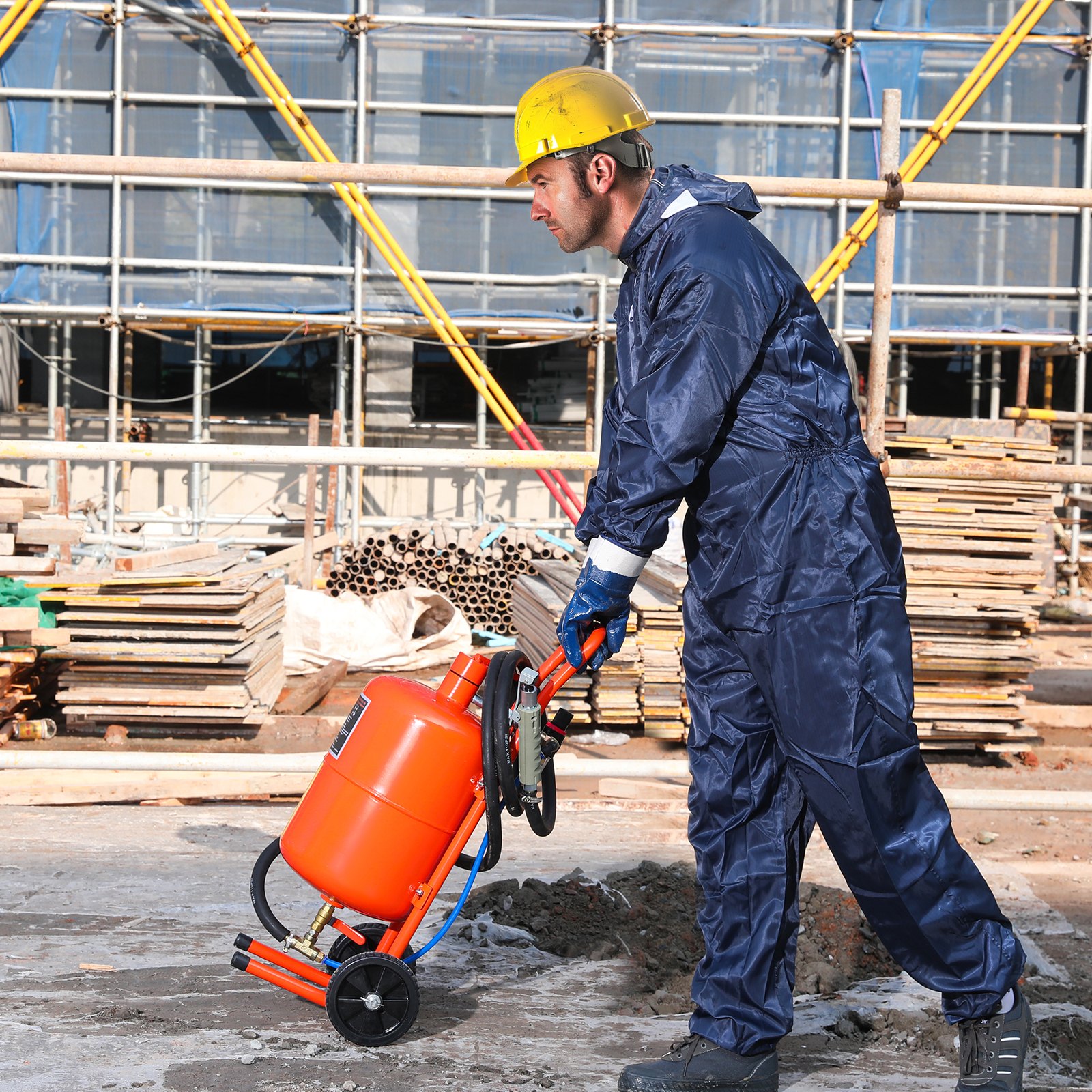 Trabajador con equipo de protección que utiliza una máquina pulidora de arena VEVOR en un sitio de construcción con andamios al fondo.