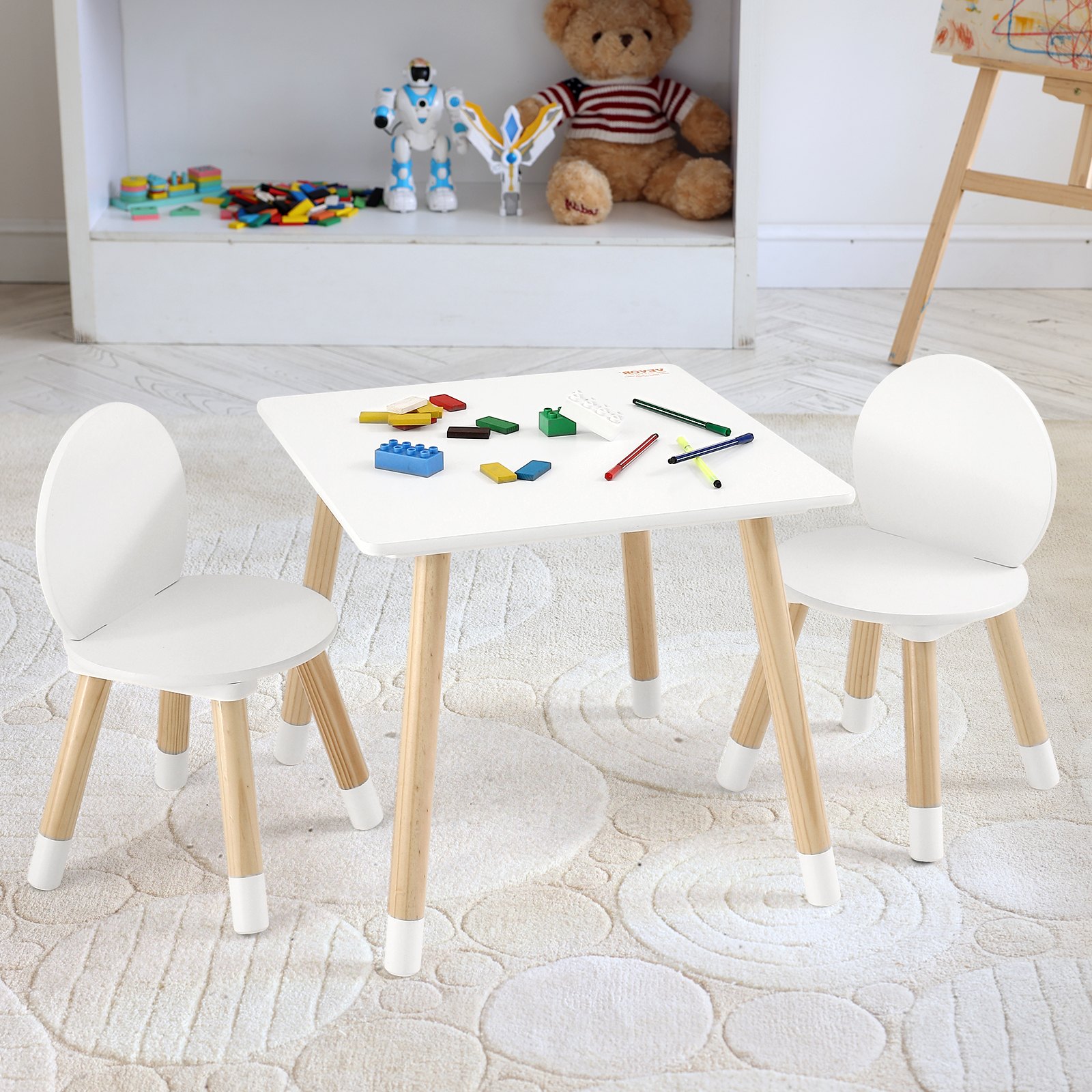 Juego de mesa para niños VEVOR con dos sillas blancas, bloques de construcción de colores, crayones y juguetes en una sala de juegos.