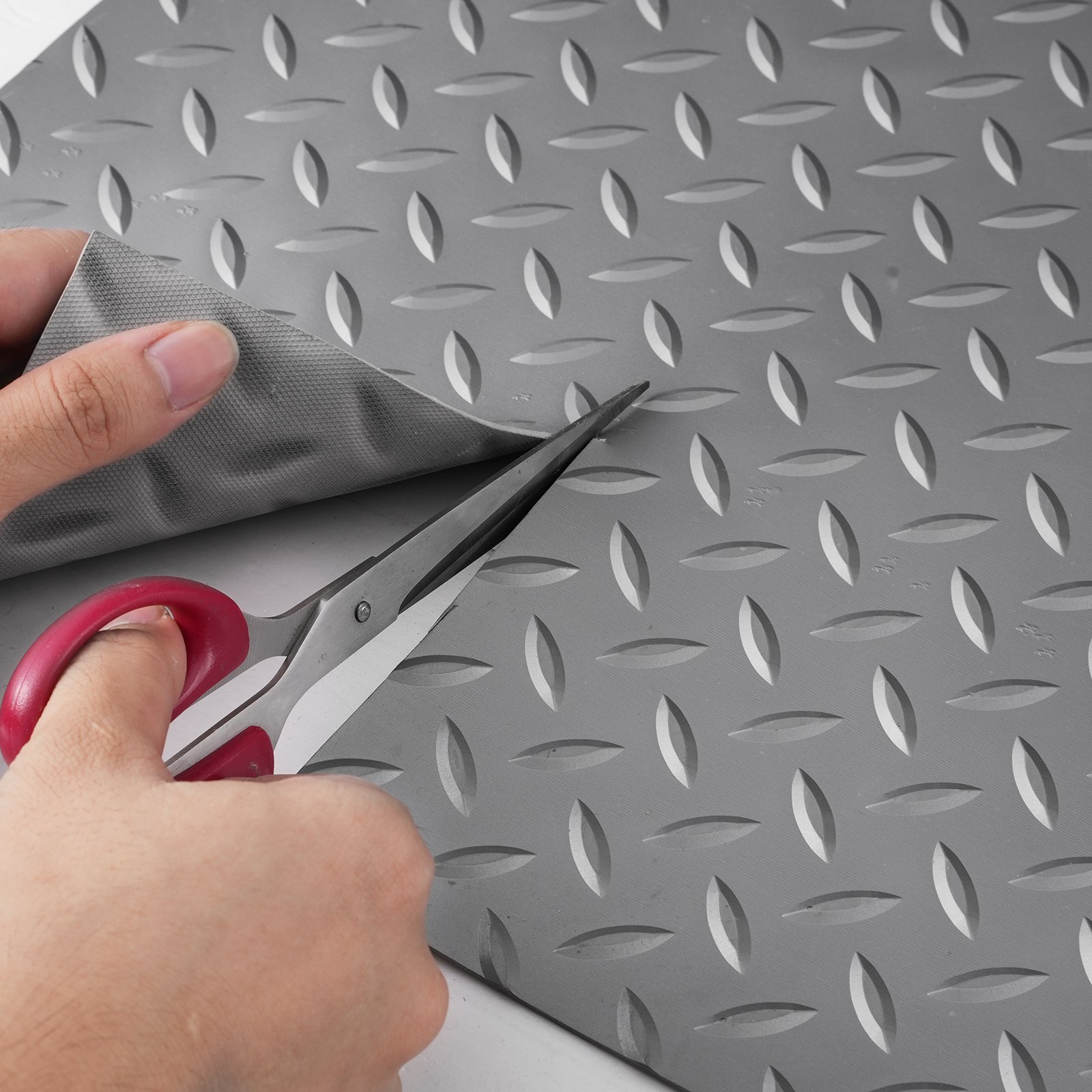 Cortando una alfombra de garaje VEVOR con tijeras, mostrando la textura de la placa de diamante.