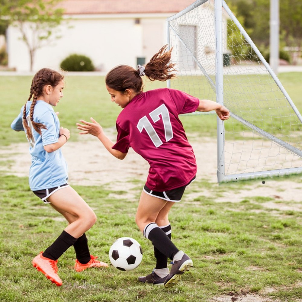 Niñas jugando al fútbol cerca de una portería de fútbol portátil VEVOR en un campo de césped.