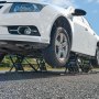 Coche blanco elevado sobre un elevador portátil VEVOR, mostrando los robustos soportes metálicos del equipo.