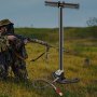 Bomba de aire PCP VEVOR en un campo con rifle y figura camuflada al fondo.