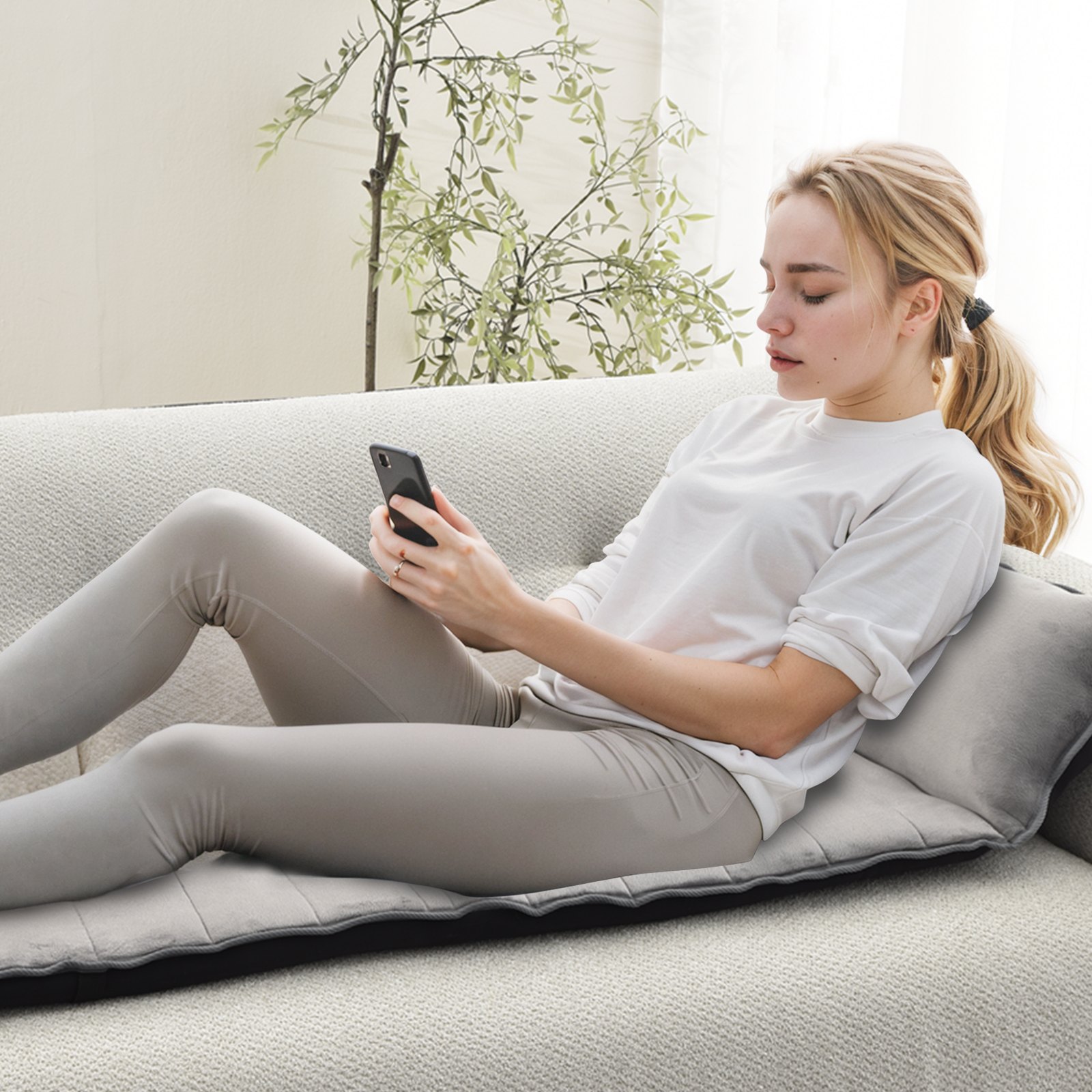 Mujer relajándose en un cojín de masaje de cuerpo completo VEVOR mientras usa un teléfono inteligente en un sofá.