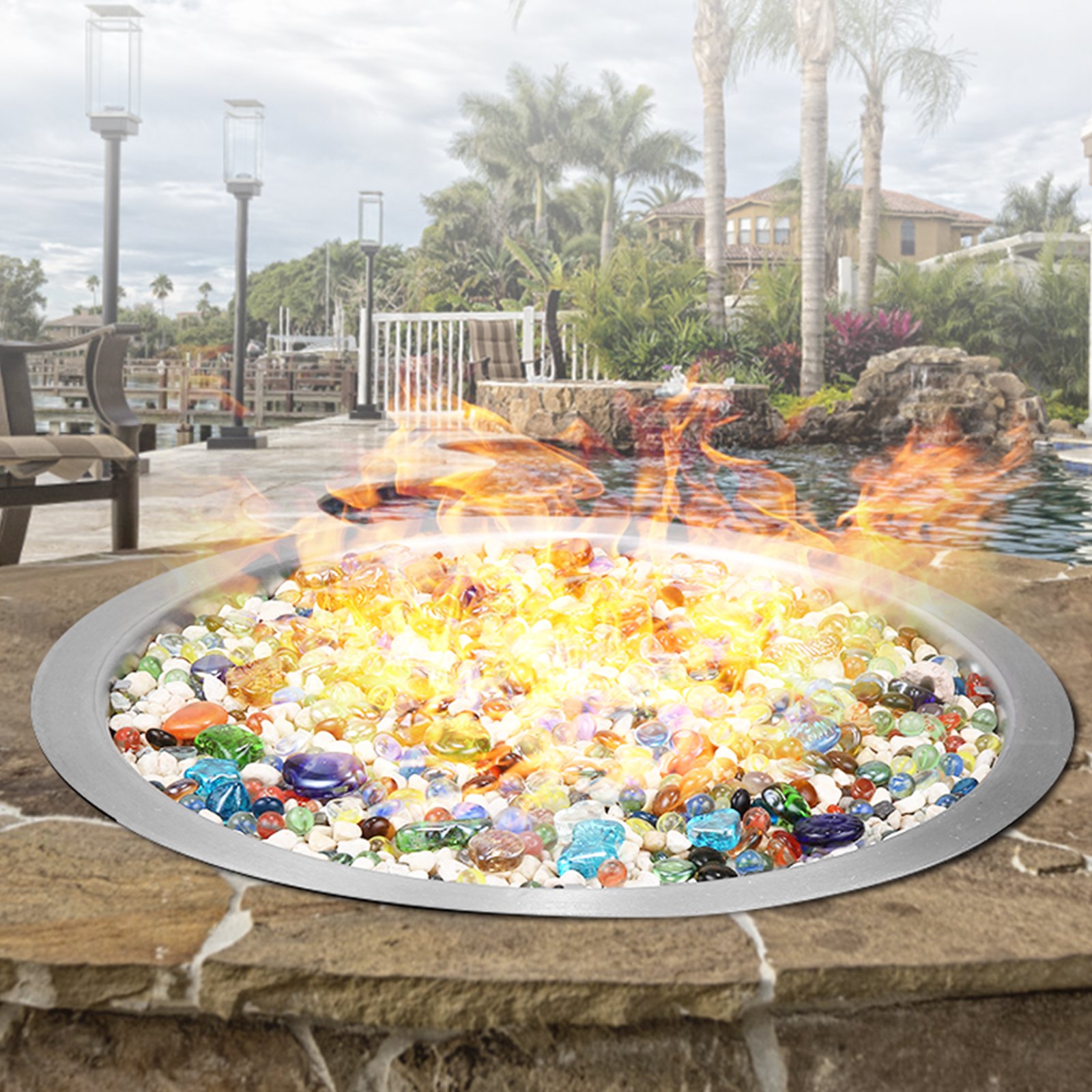 Brasero VEVOR con piedras de colores y llamas en un lujoso entorno al aire libre junto a la piscina.