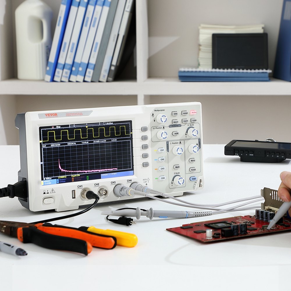 Osciloscopio digital VEVOR que muestra formas de onda junto a herramientas en un escritorio blanco, con estantes en el fondo.