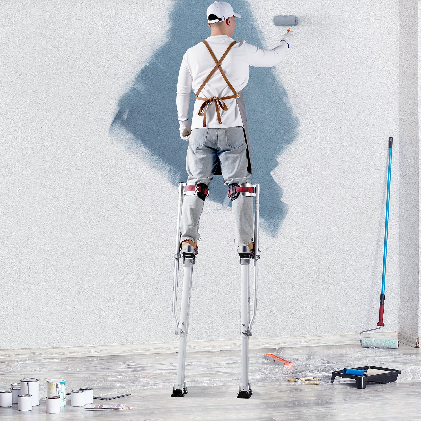 pintor sobre zancos de yeso VEVOR pintando una pared, rodeado de suministros de pintura en el suelo.
