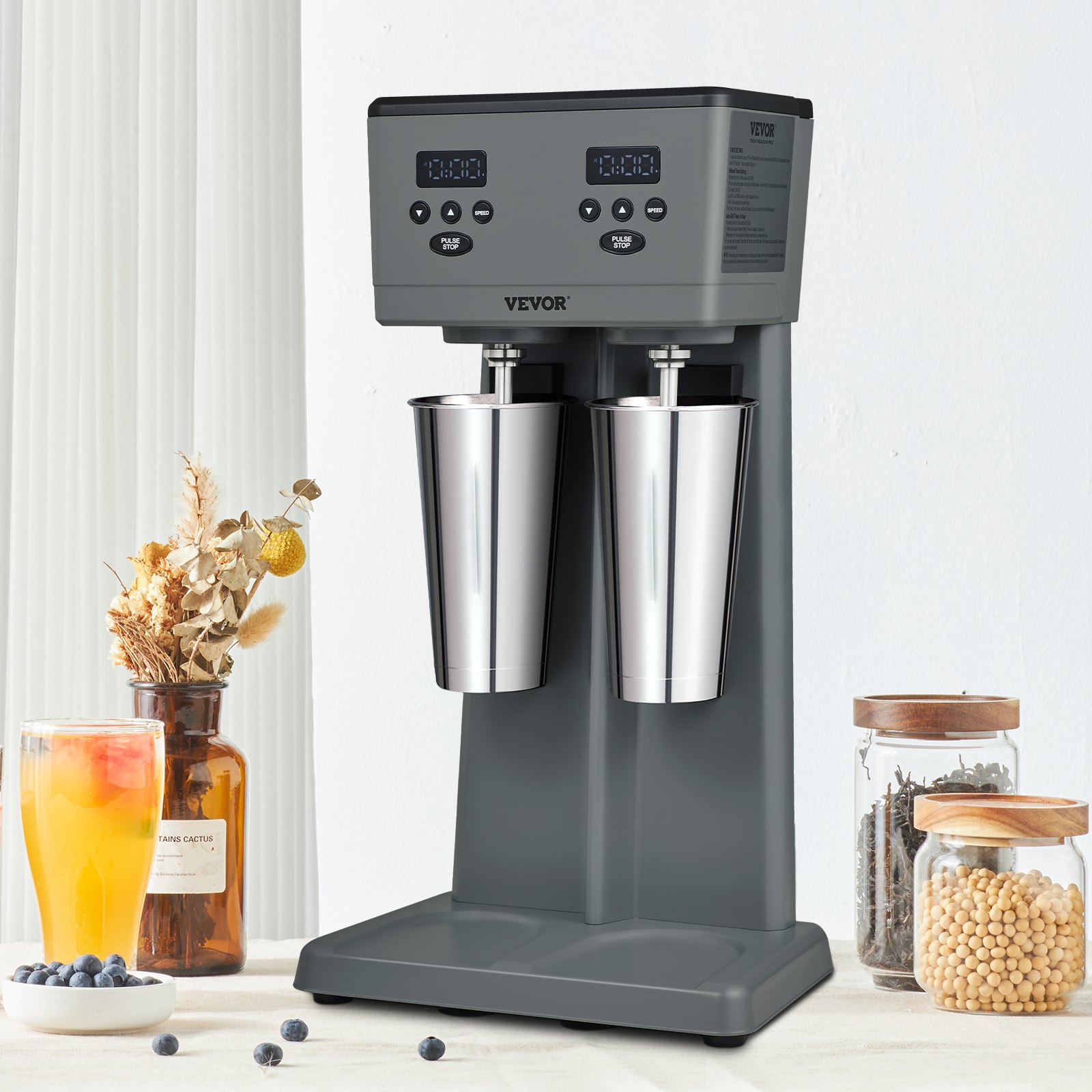 Máquina para hacer batidos VEVOR con vasos mezcladores dobles sobre una encimera de cocina adornada con ingredientes y decoración.