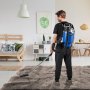 Persona que utiliza una aspiradora de mochila VEVOR sobre una alfombra de felpa en una sala de estar moderna.