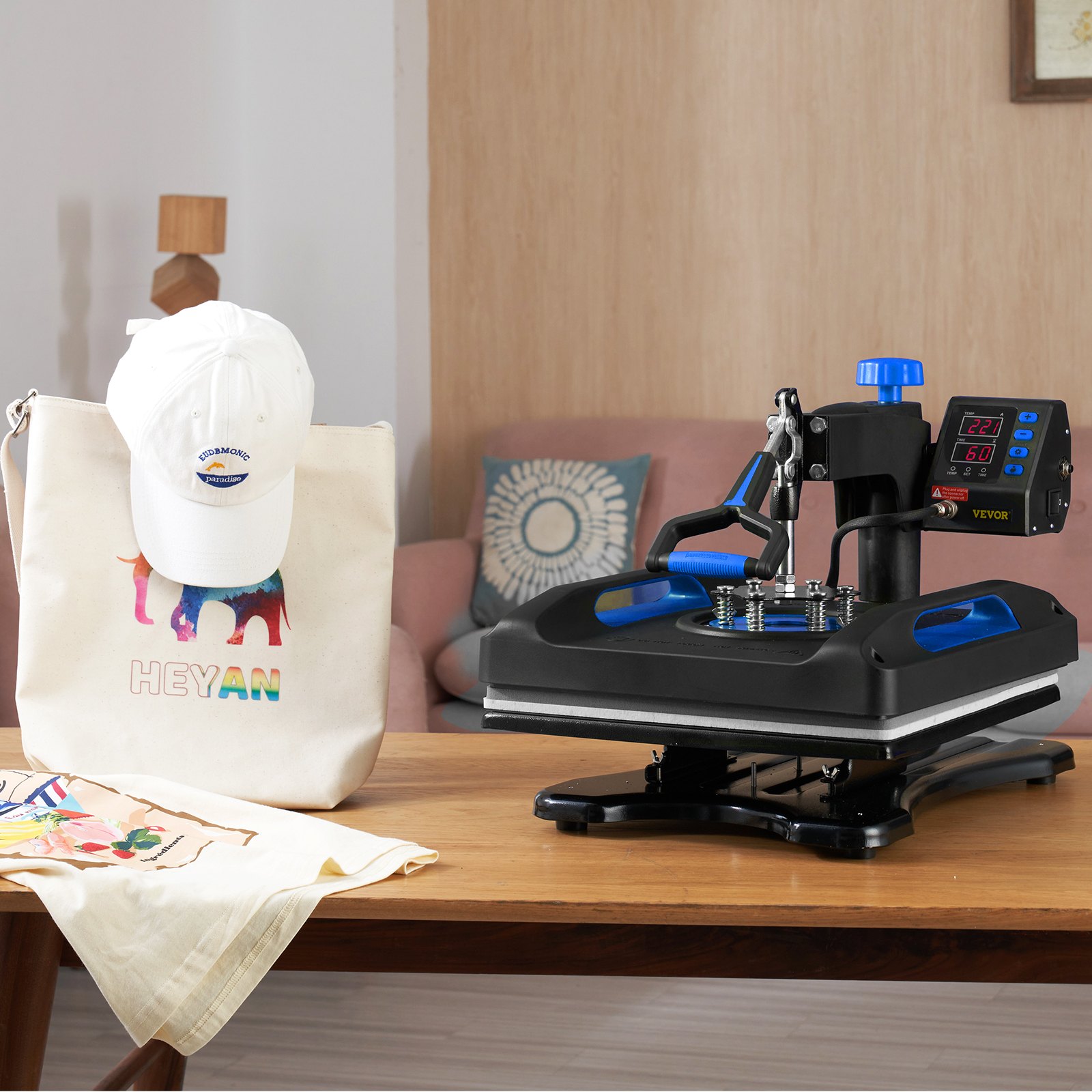 Máquina de prensado térmico VEVOR sobre una mesa de madera con una tapa y una bolsa de mano impresas artesanalmente.