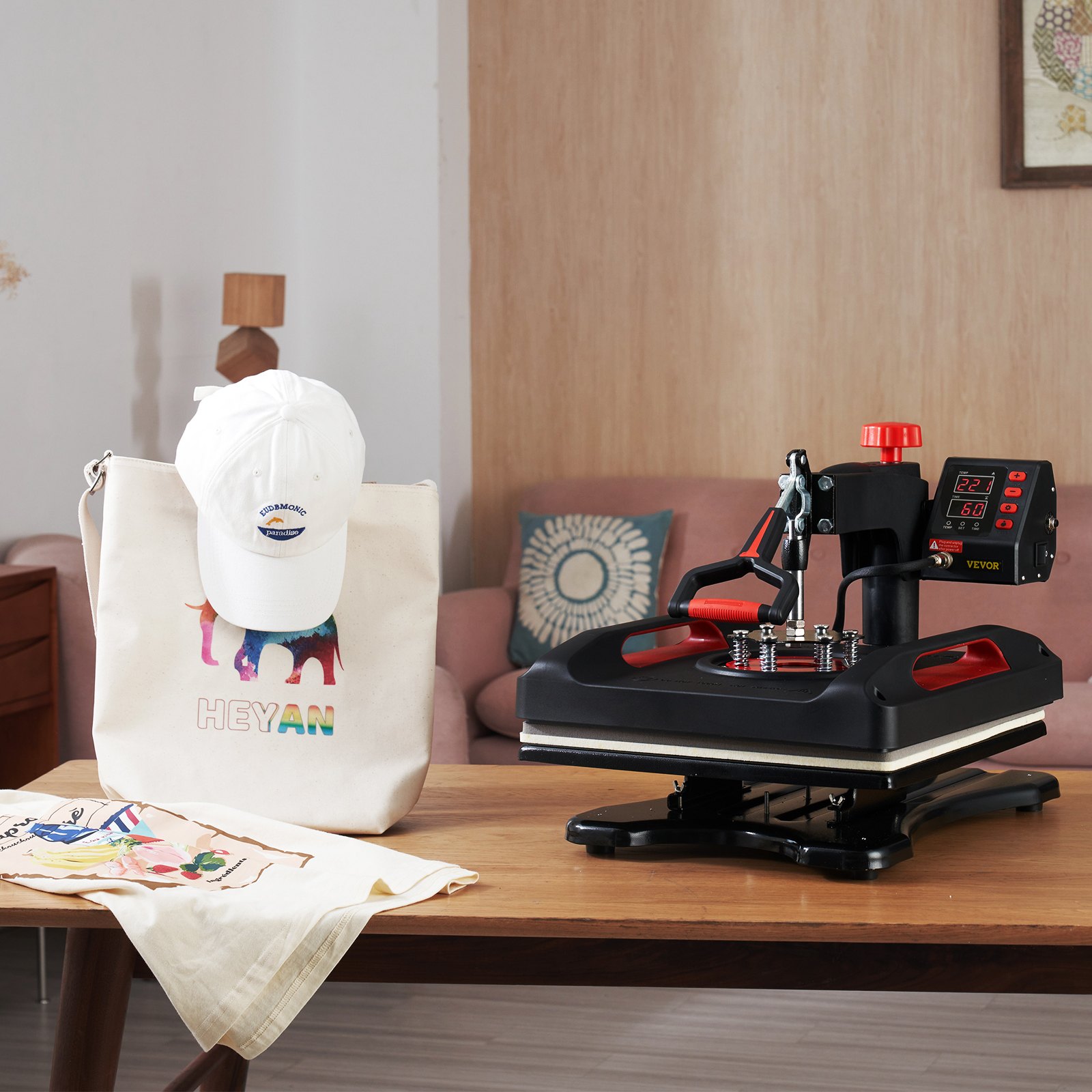 Máquina de prensado térmico VEVOR sobre una mesa de madera con bolsa de mano, sombrero y tela personalizados.