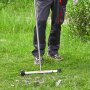 Persona que utiliza una barredora magnética VEVOR en un área con césped para recoger residuos metálicos.