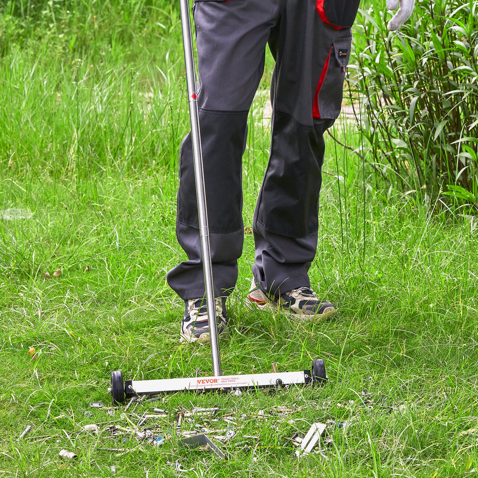 Persona que utiliza una barredora magnética VEVOR en un área con césped para recoger residuos metálicos.