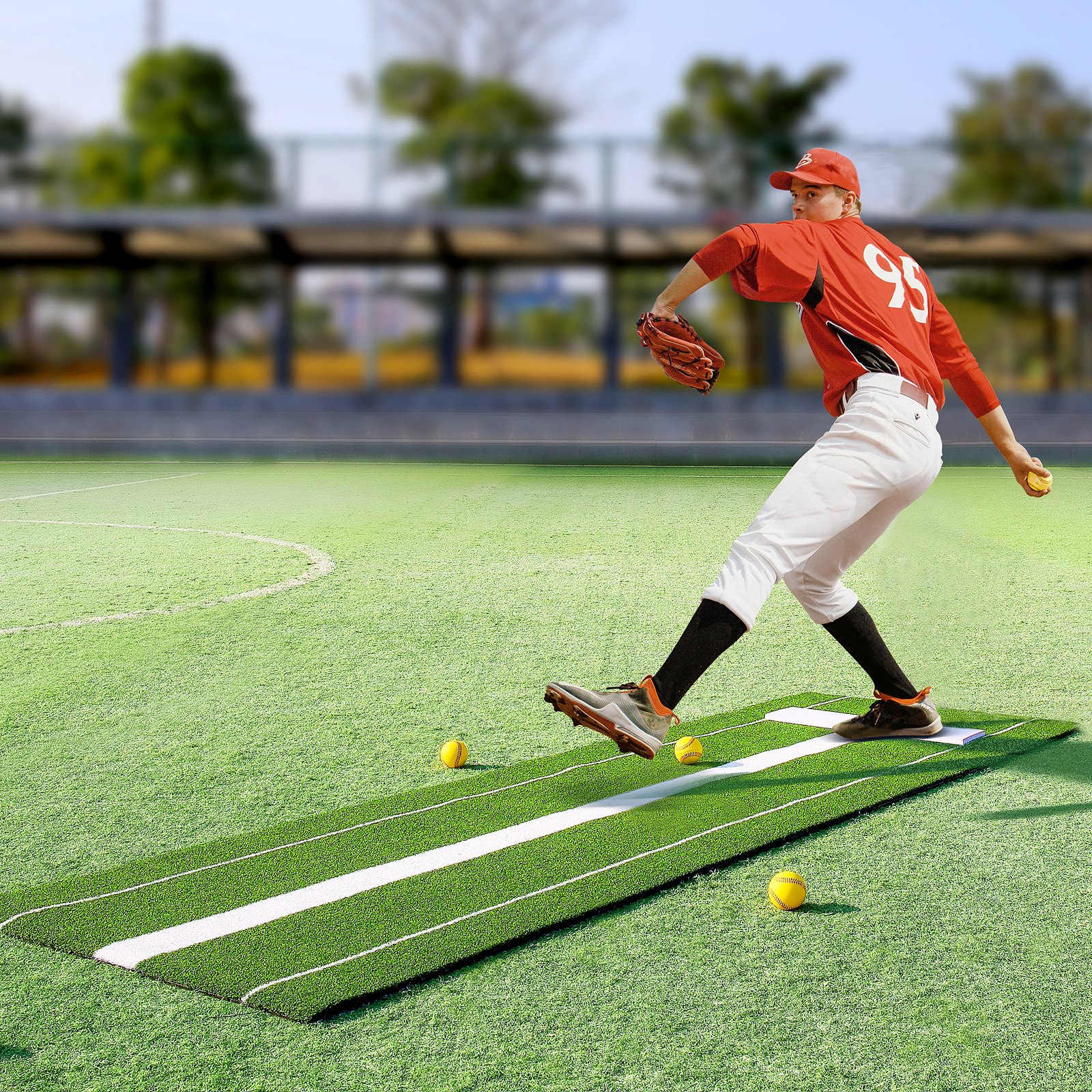 lanzador con uniforme rojo practicando en el tapete de lanzamiento de softbol VEVOR con pelotas de softbol amarillas en un campo verde.