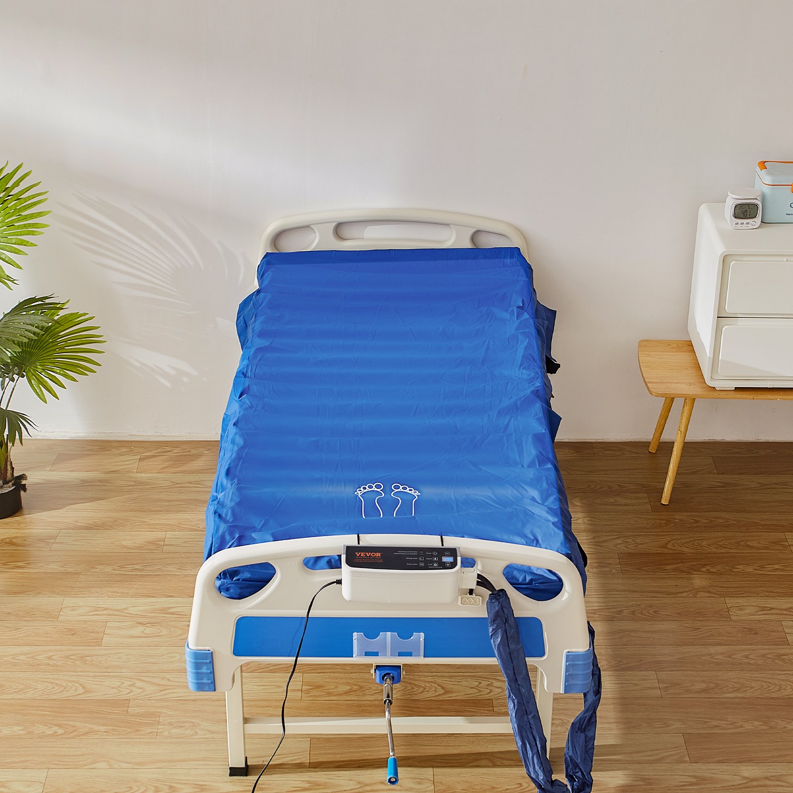 Colchón de presión de aire VEVOR sobre una cama de hospital con unidad de control, rodeado de una decoración clara y suelo de madera.