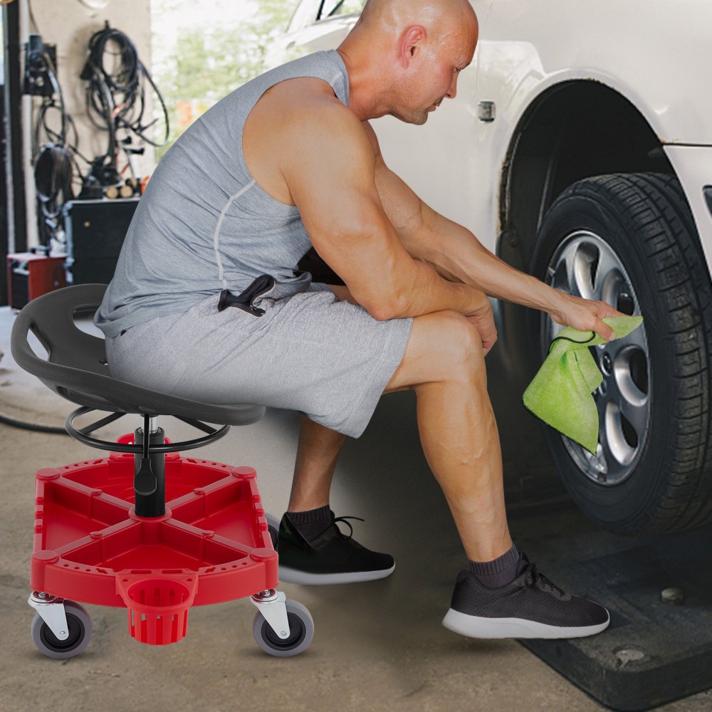 Hombre que usa un taburete de garaje con ruedas VEVOR para limpiar las ruedas del coche con un paño verde.