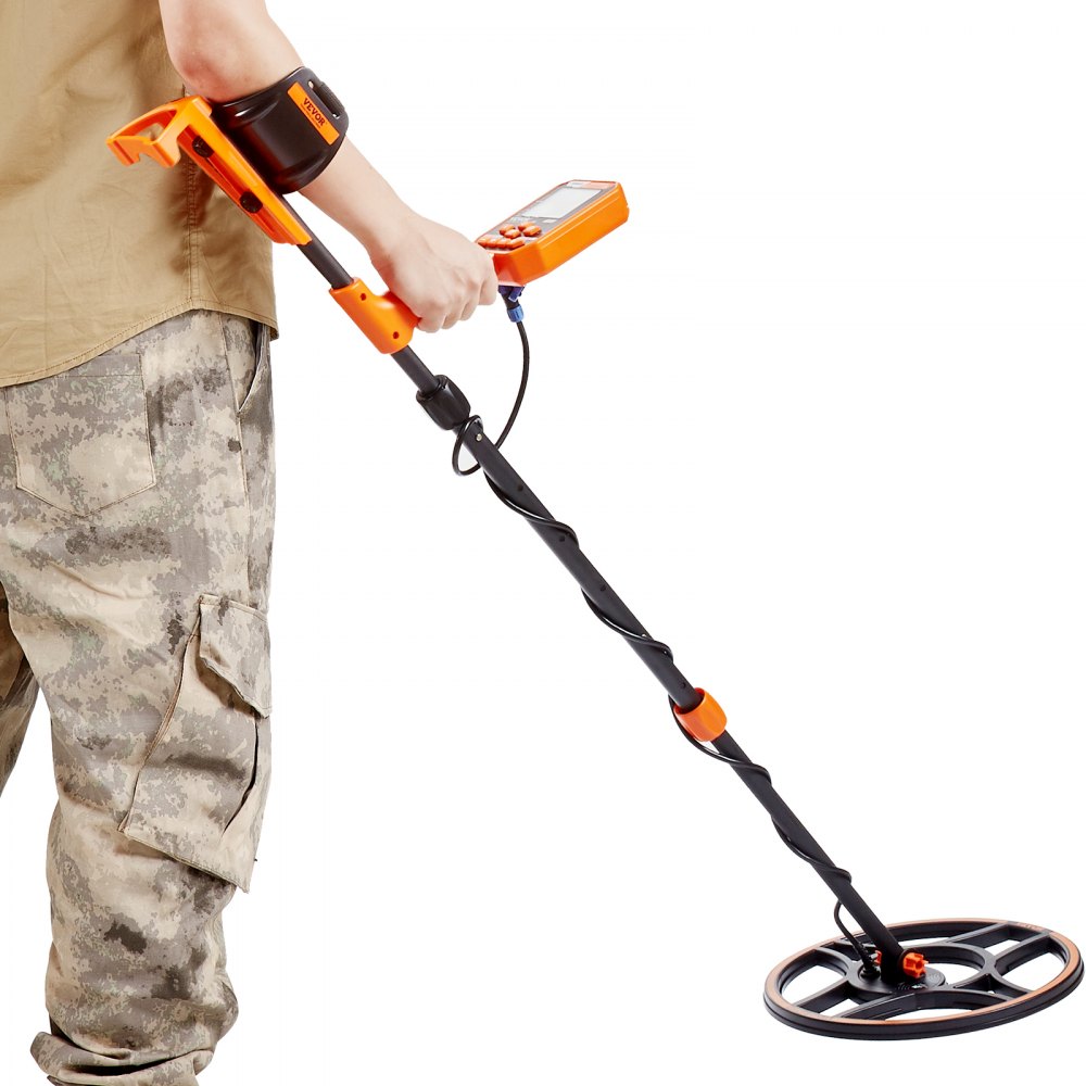 Persona que utiliza un detector de metales impermeable VEVOR con pantalones de camuflaje con panel de control y bobina visibles.