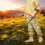 Persona que utiliza un detector de metales resistente al agua VEVOR en un campo de hierba al atardecer, con montañas al fondo.