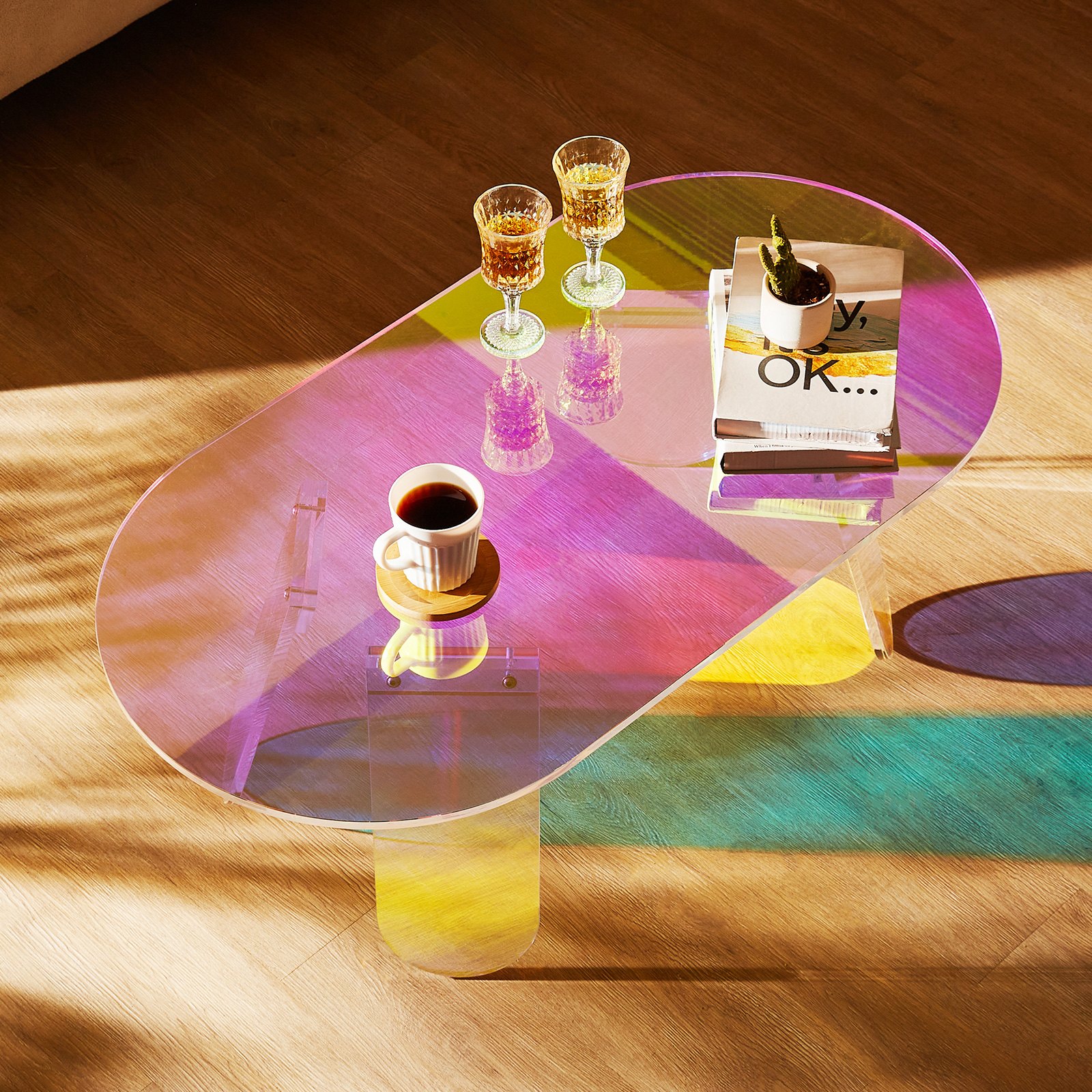 Mesa de centro de acrílico VEVOR con reflejos coloridos, cubierta con vasos, libros y una taza de café.