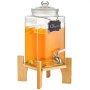 Dispensador de bebidas de vidrio VEVOR lleno de líquido de naranja y rodajas de limón sobre un soporte de madera.