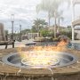 Brasero VEVOR junto a una piscina con palmeras, sillas de patio y un moderno entorno al aire libre.