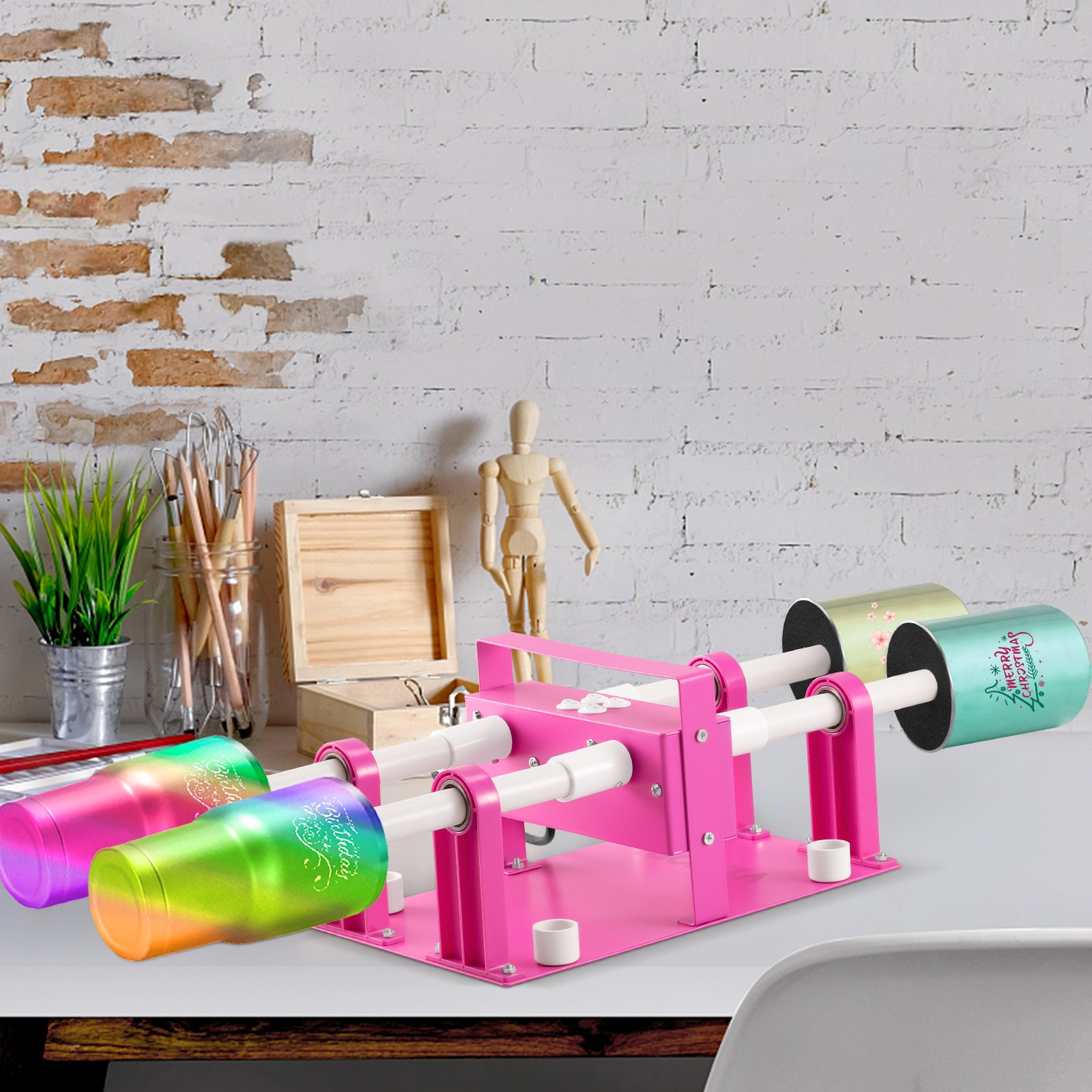 Volteador de tazas VEVOR rosa para 4 tazas sobre un escritorio con vasos coloridos, materiales de arte y un maniquí contra una pared de ladrillos.