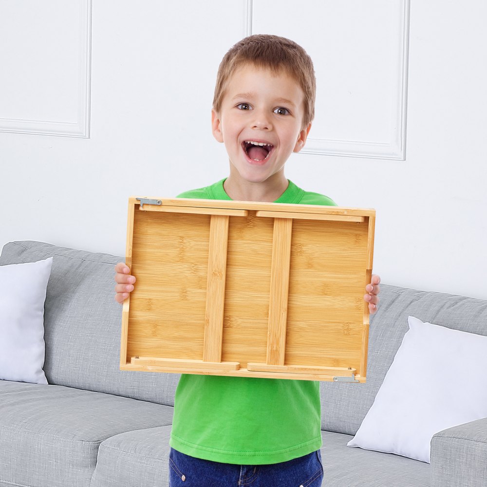 Niño sosteniendo una mesa de cama VEVOR con un sofá gris y cojines blancos en el fondo.