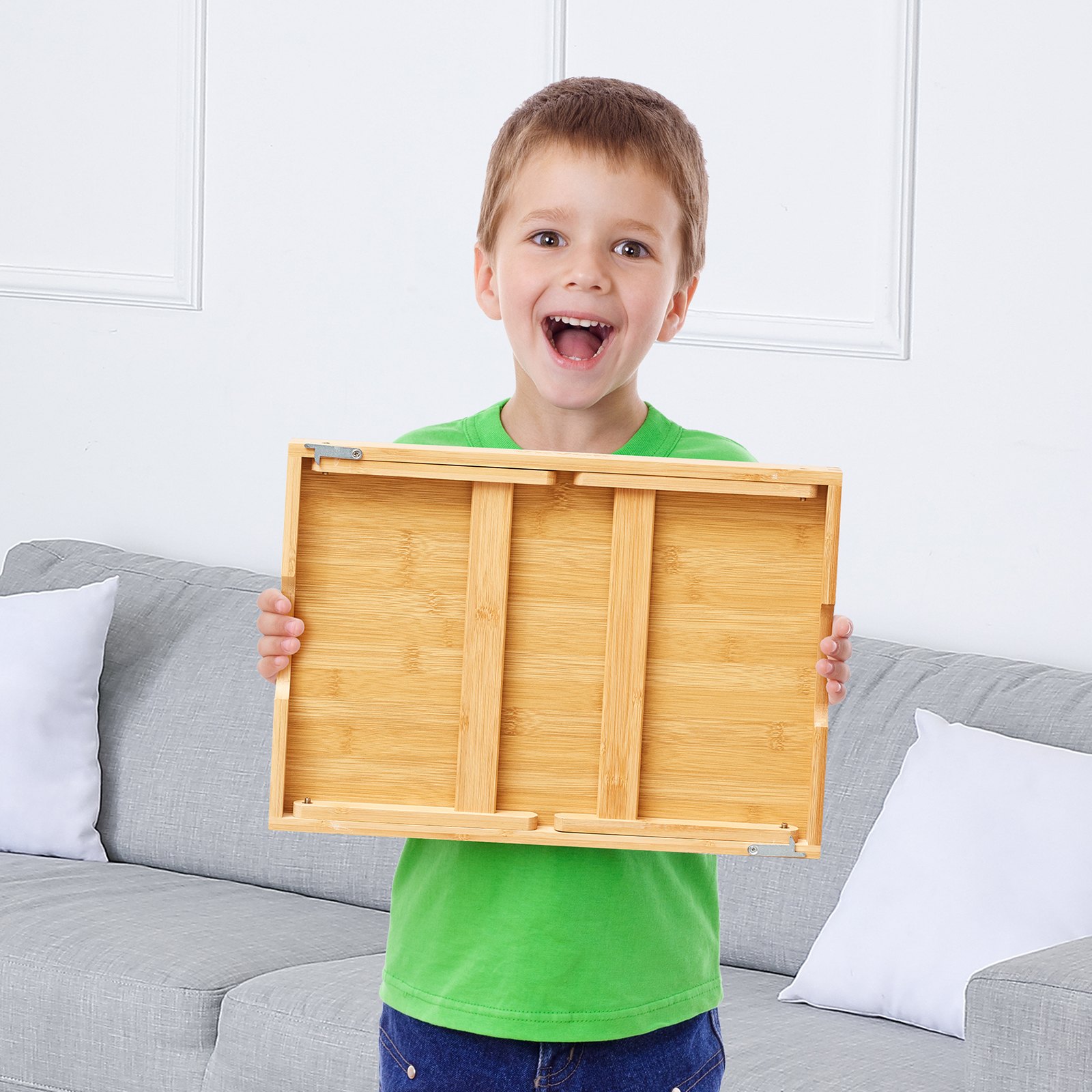 Niño sosteniendo una mesa de cama VEVOR con un sofá gris y cojines blancos en el fondo.