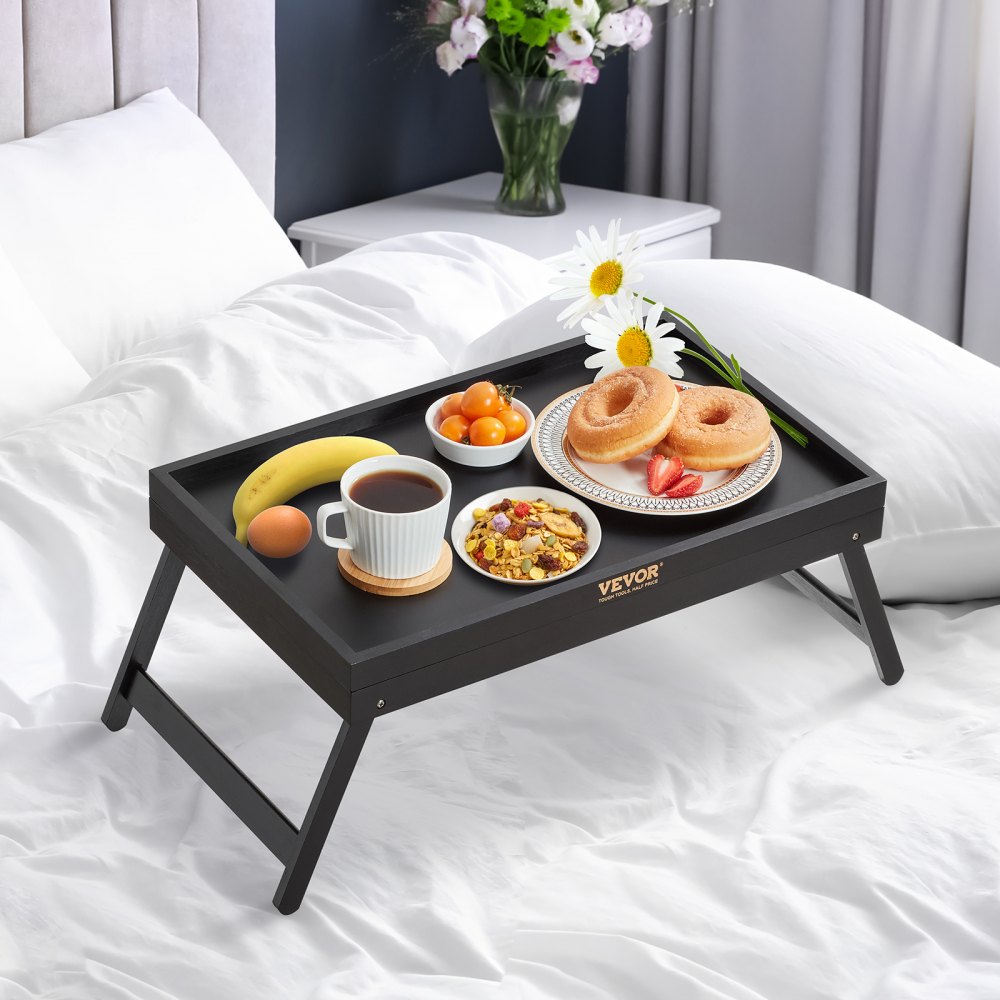 Mesa bandeja de cama VEVOR sobre una cama blanca, que contiene un desayuno con donas, fruta, café y flores.