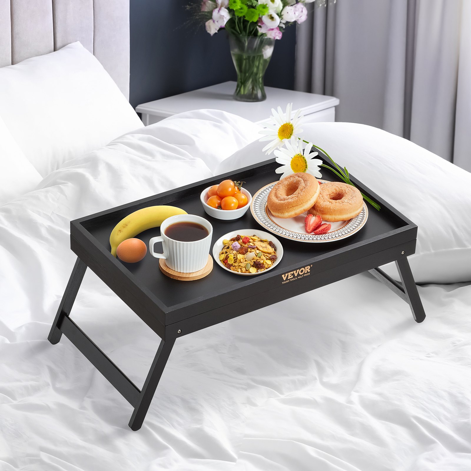 Mesa bandeja de cama VEVOR sobre una cama blanca, que contiene un desayuno con donas, fruta, café y flores.