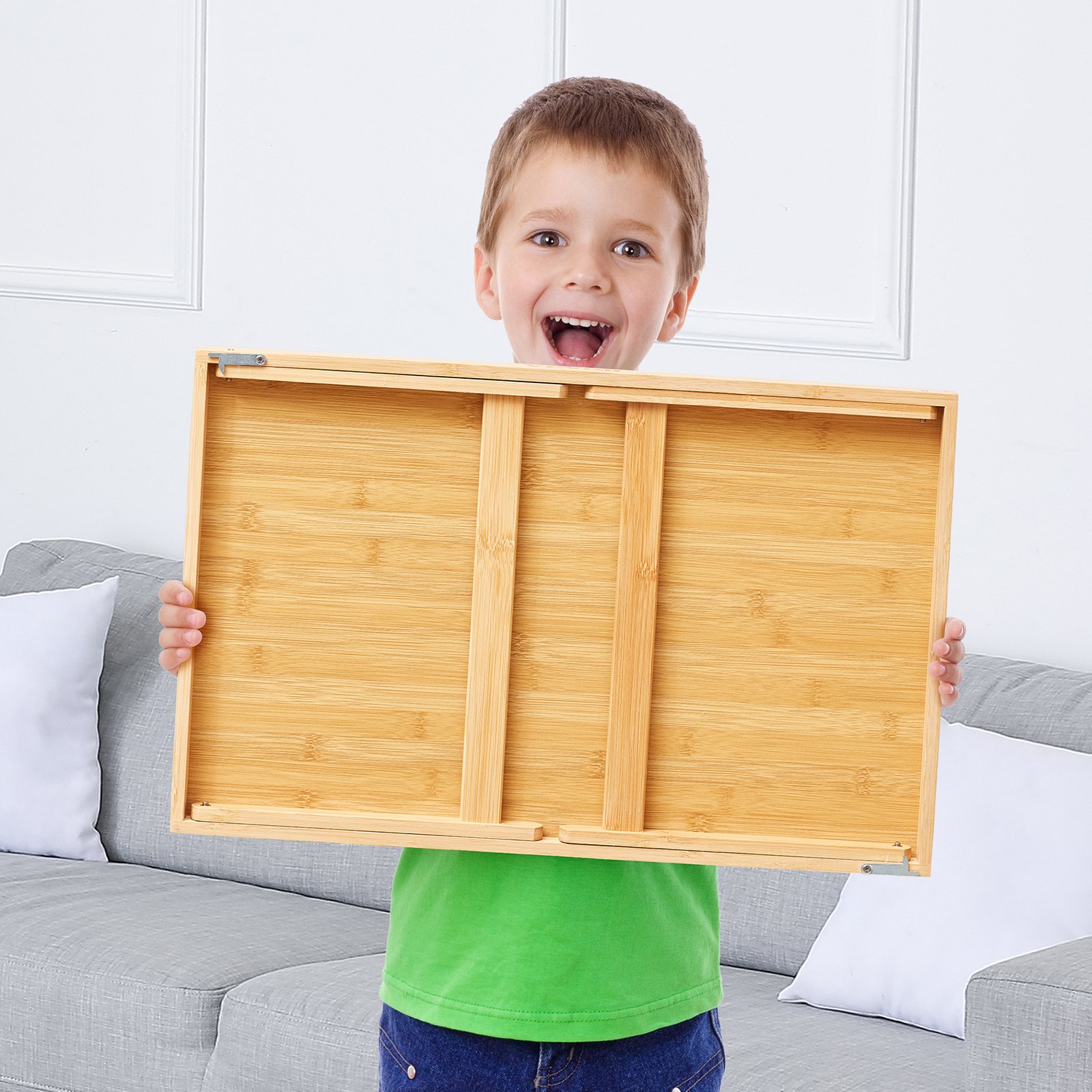 Niño sosteniendo una mesa de cama VEVOR en una sala de estar con un sofá gris al fondo.