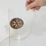 mano sosteniendo una cubierta de mesa transparente VEVOR sobre una taza blanca y un platillo con una cuchara.