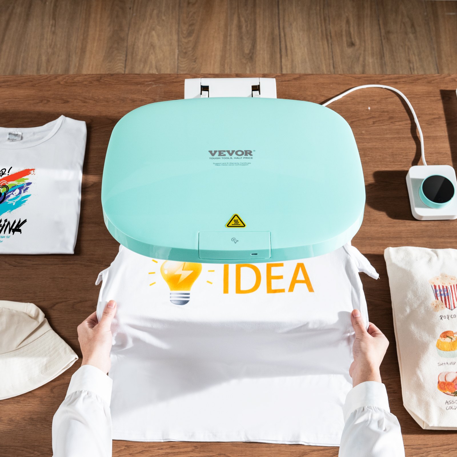 Impresión automática con prensa térmica VEVOR &quot;idea&quot; sobre una camiseta blanca, con accesorios sobre una mesa de madera.