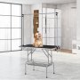 Perro en una mesa de peluquería para mascotas VEVOR en una habitación moderna y luminosa con grandes ventanales y paredes de azulejos.
