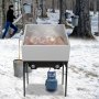 Bandeja evaporadora de jarabe de arce VEVOR en un bosque nevado con árboles perforados y jarabe hirviendo.