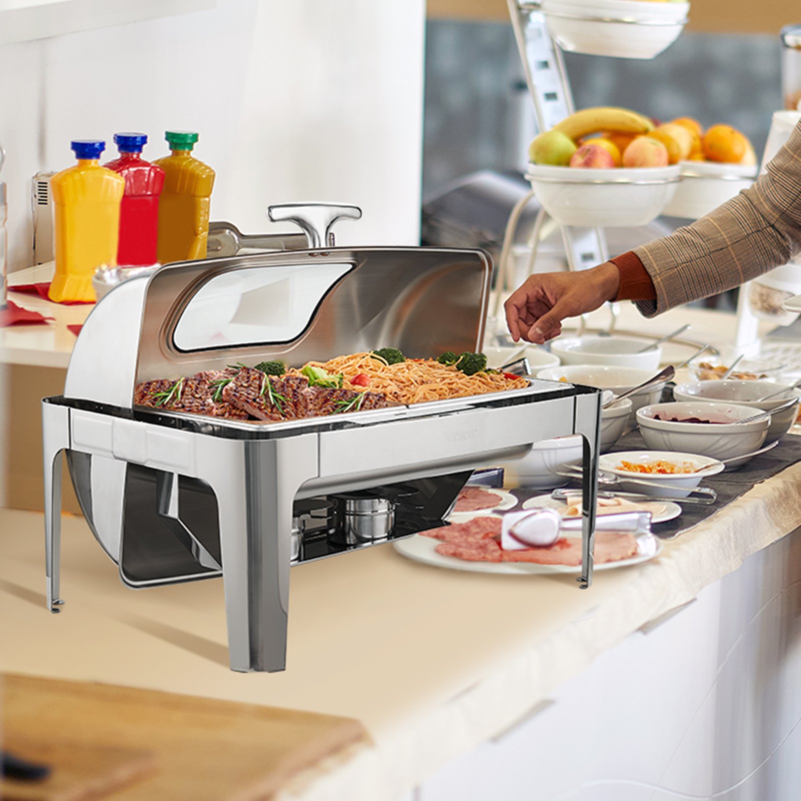 configuración de buffet con un chafing dish VEVOR lleno de pasta y carne, rodeado de condimentos y frutas.