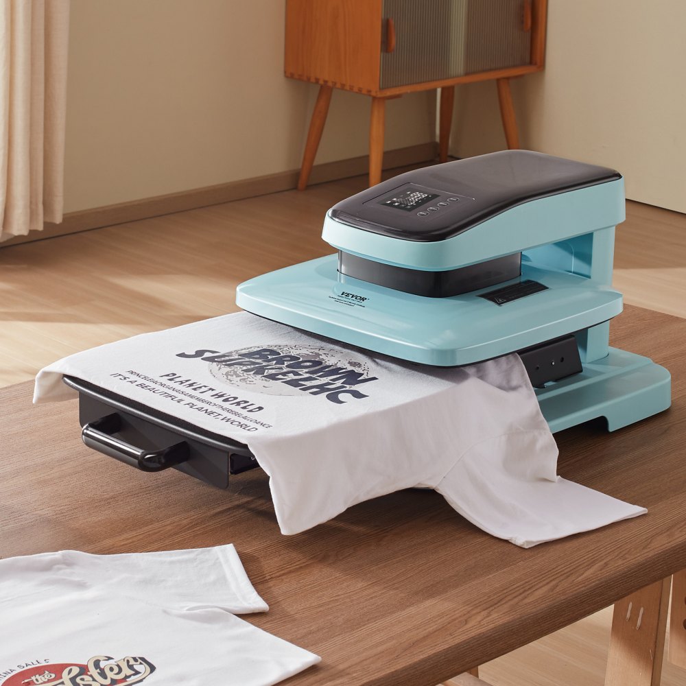Máquina de prensado térmico automática VEVOR sobre una mesa de madera imprimiendo una camiseta blanca con texto en una habitación llena de luz.