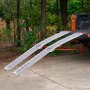 Rampas de carga de aluminio VEVOR unidas a un camión naranja, que se extienden hasta el hormigón con árboles al fondo.