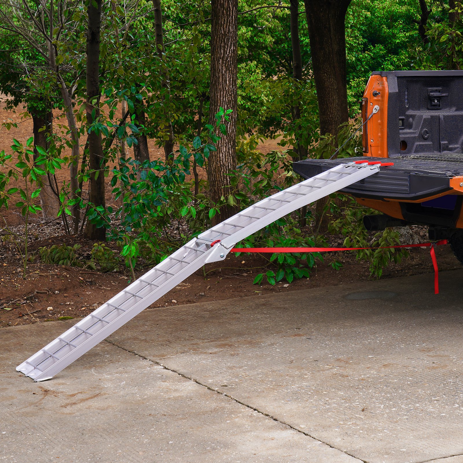 Rampa de carga para motocicleta VEVOR de aluminio unida a la plataforma de un camión naranja delante de un fondo de bosque.