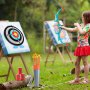 child playing with VEVOR kids archery set outdoors, aiming at target boards with arrows by her side.