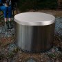 VEVOR fire pit cover on a stainless steel fire pit outdoors with a person sitting nearby.