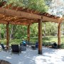 pergola with wooden beams supported by VEVOR post base brackets, outdoor seating, and green backyard.