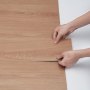handen die VEVOR zelfklevende vinylvloertegels met een houtnerfstructuur installeren.
